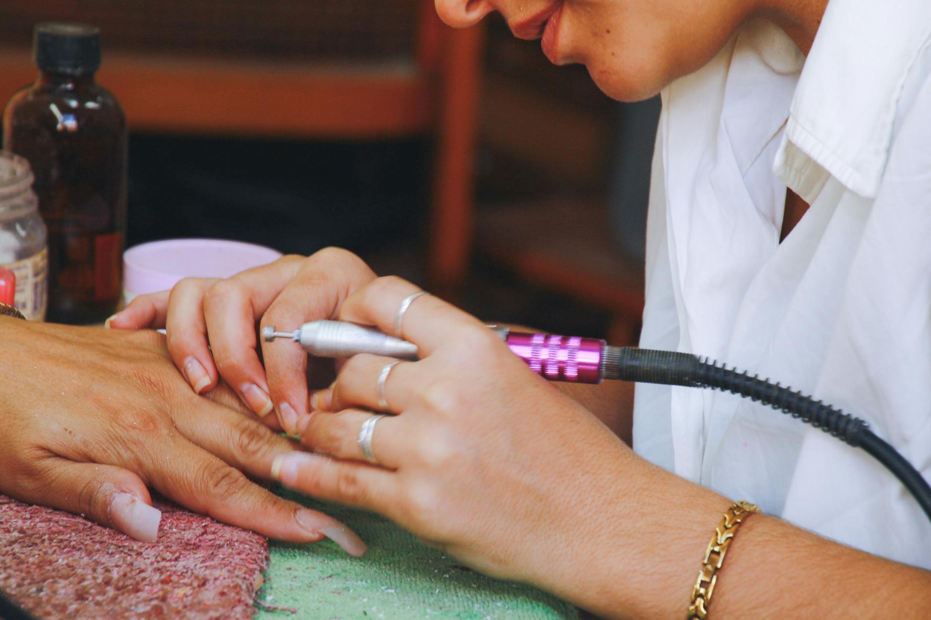 Stylistka opracowuje paznokieć frezarką podczas manicure hybrydowego