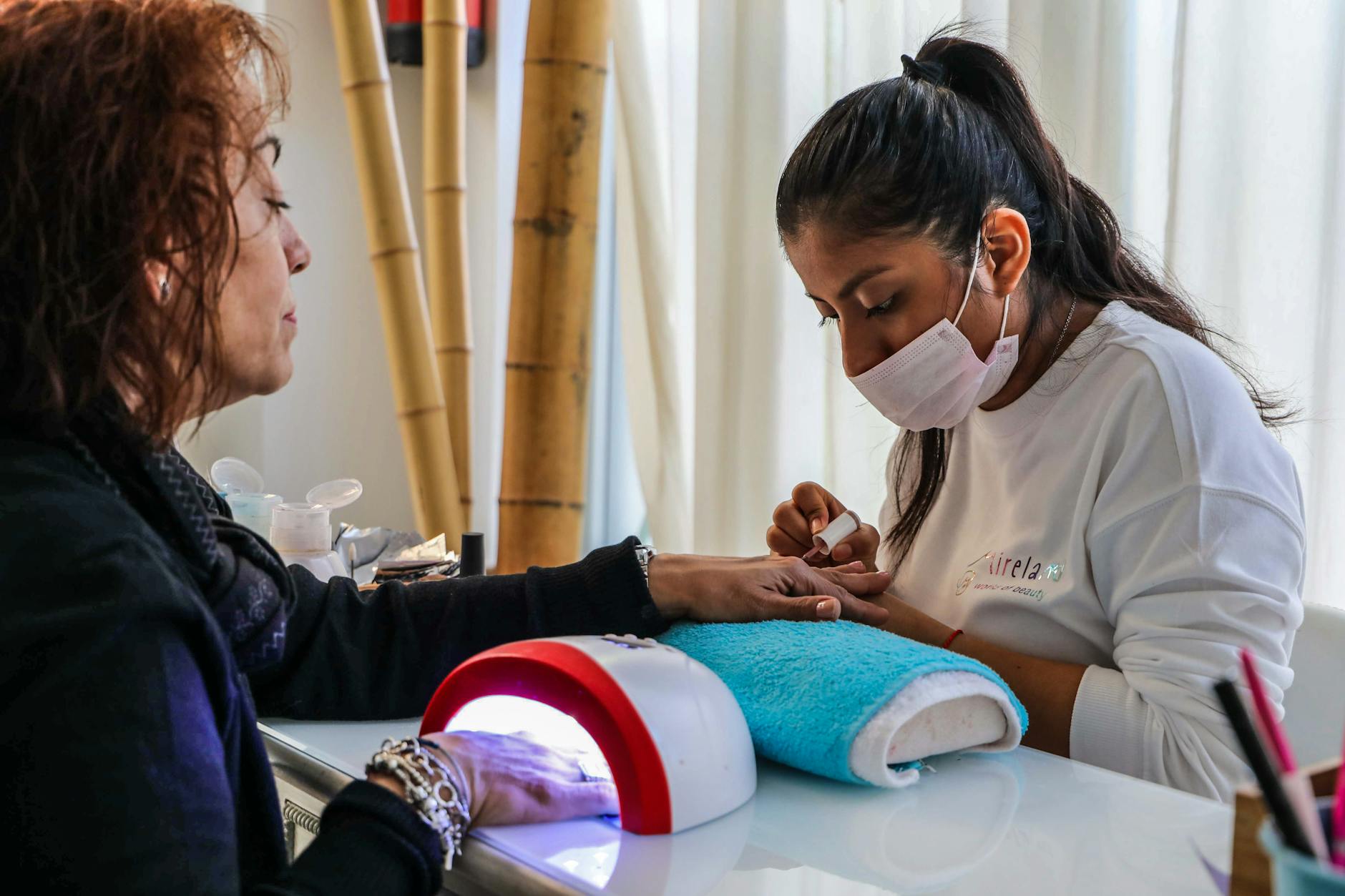 Stylistka wykonuje manicure klientce przy lampie w salonie kosmetycznym
