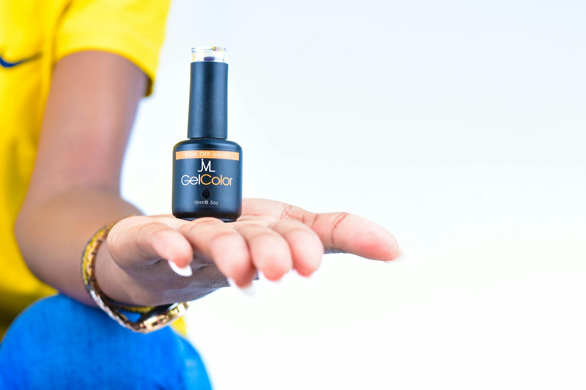 Przyczepność żelu: jak wpływa na nią odtłuszczacz, dehydrator i primer Dłoń kobiety prezentująca buteleczkę lakieru żelowego na jasnym tle