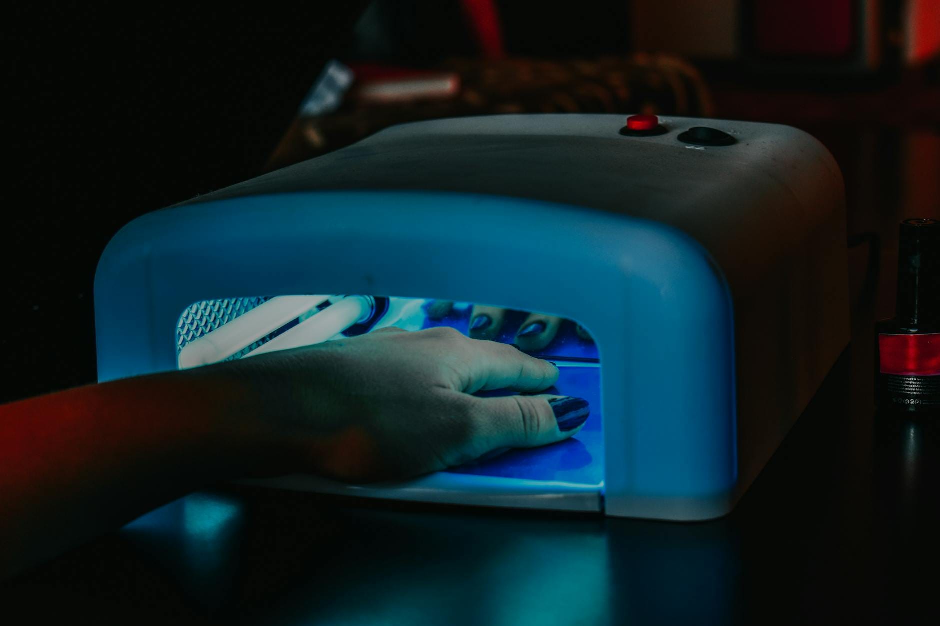 Dłoń z żelowym manicure utwardzana w niebieskiej lampie LED