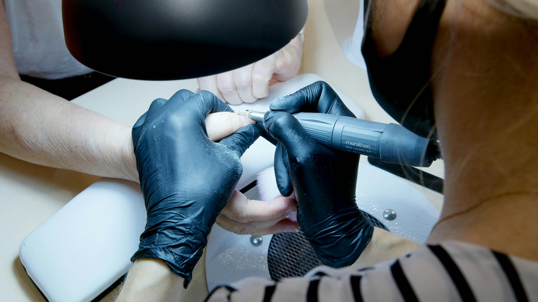 Manicurzystka wycina skórki narzędziem przy paznokciach klientki