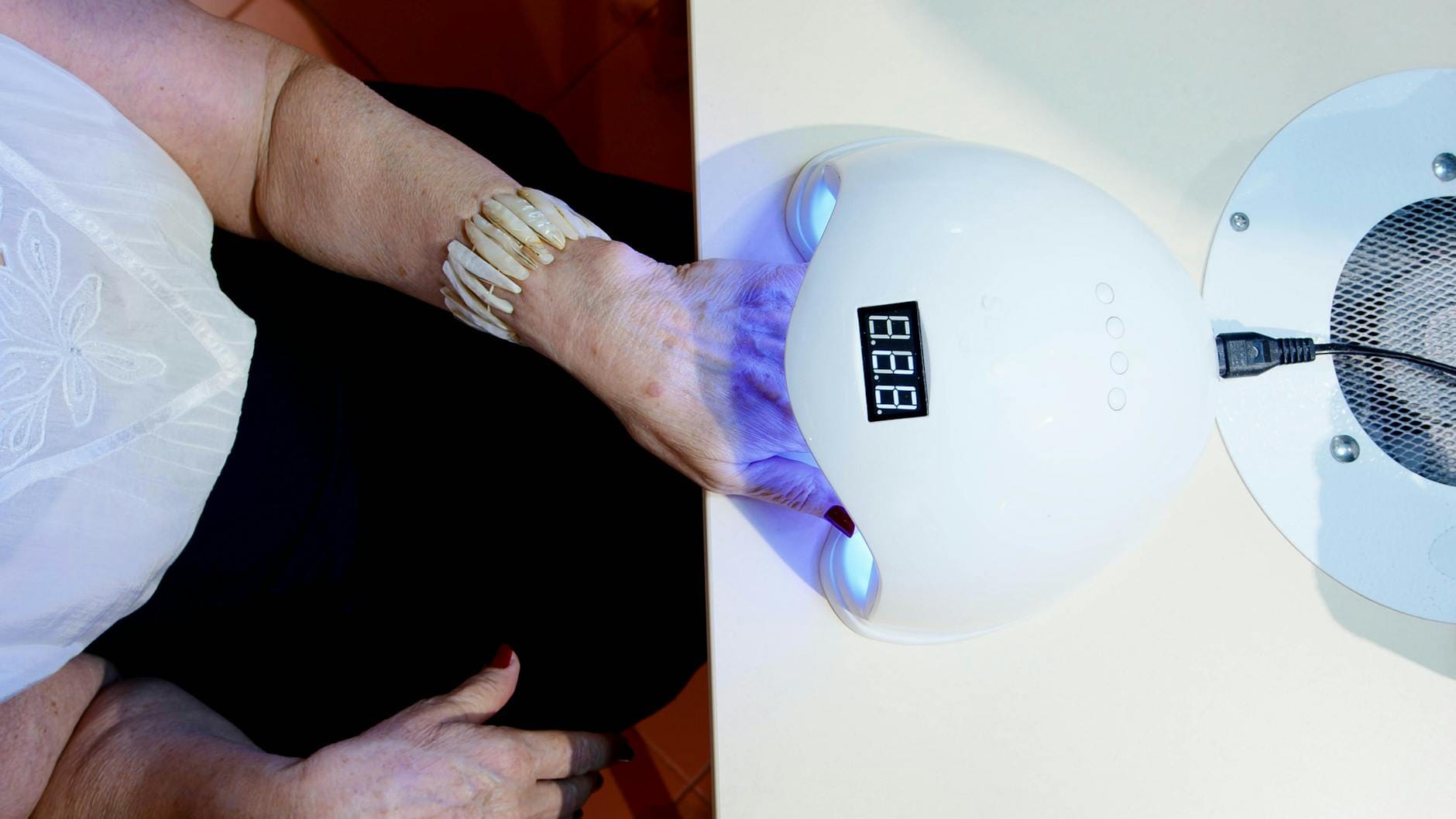 Dłoń kobiety pod lampą UV w salonie manicure