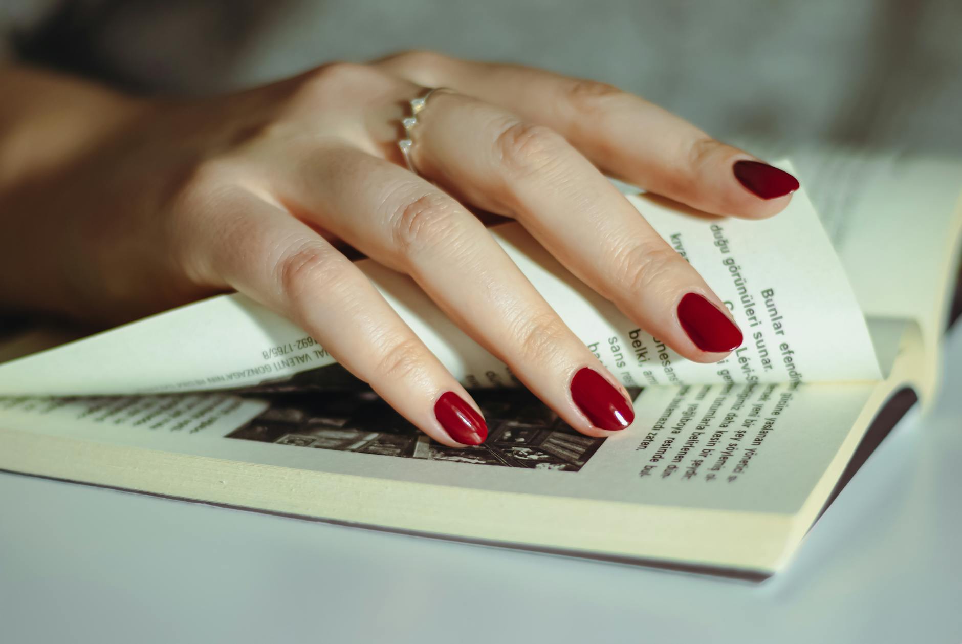 Dłoń z czerwonym manicure hybrydowym przewracająca kartki książki