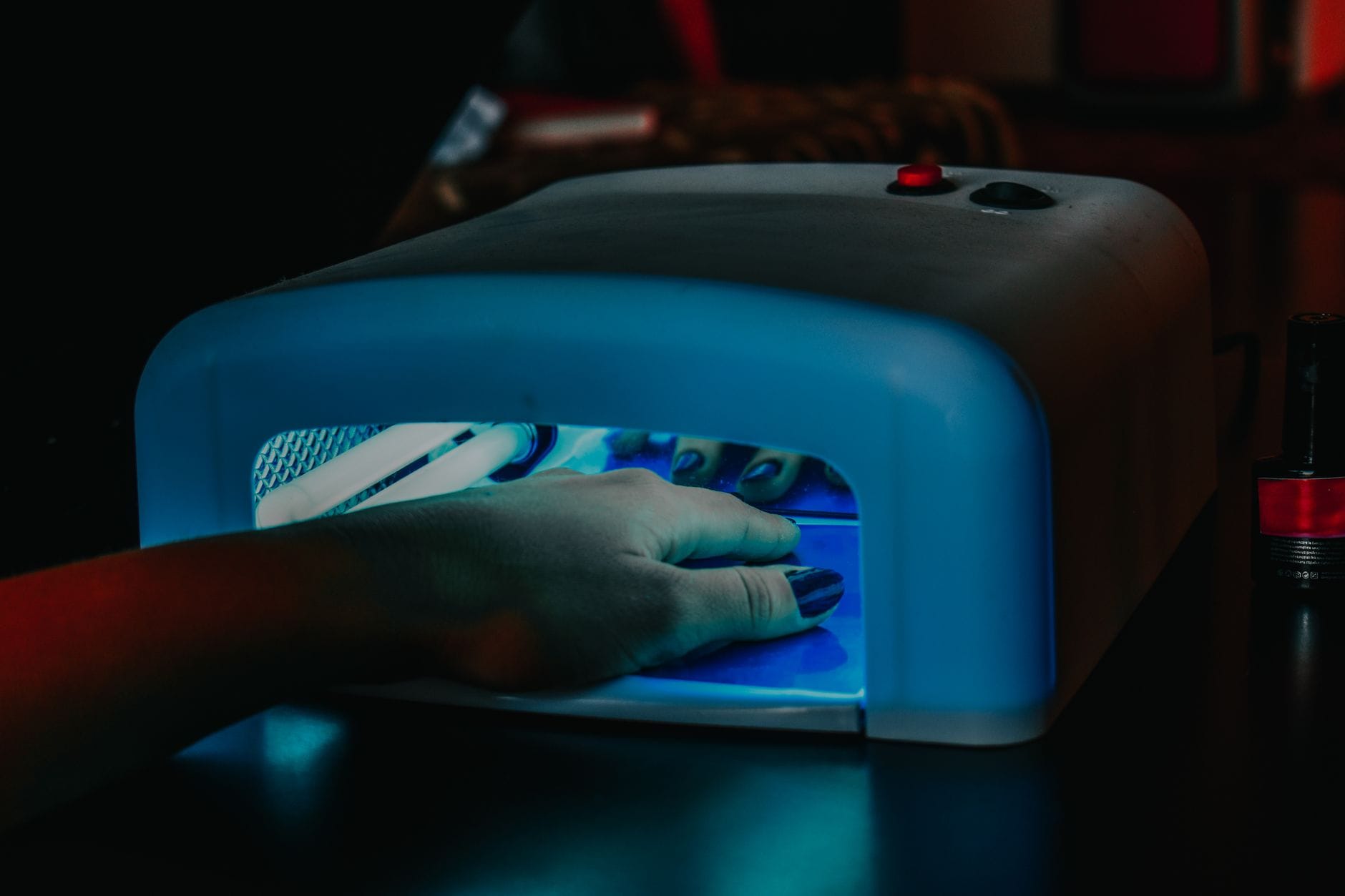 Dlaczego żel pęka na bokach? Diagnoza po kształcie pęknięcia Dłoń z manicurem żelowym pod niebieską lampą LED
