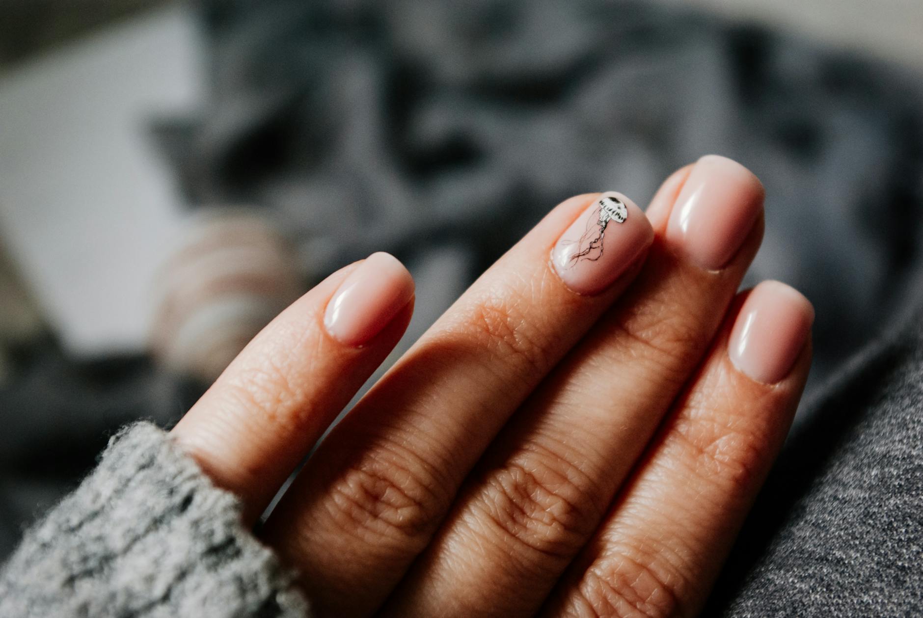 Dłonie kobiety w swetrze prezentujące paznokcie z kreatywnym manicure