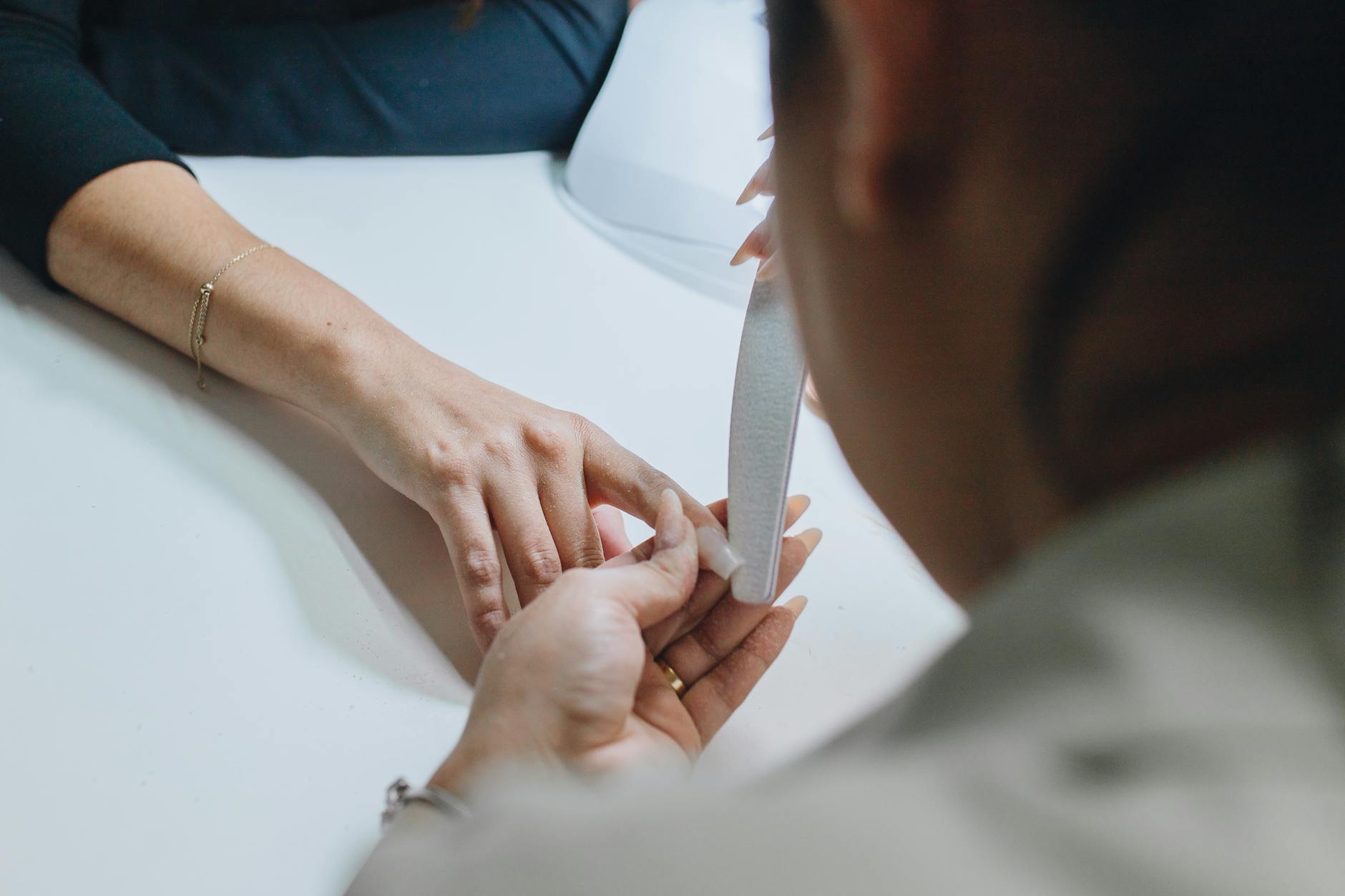 Stylistka piłuje paznokieć klientki podczas zabiegu manicure w salonie