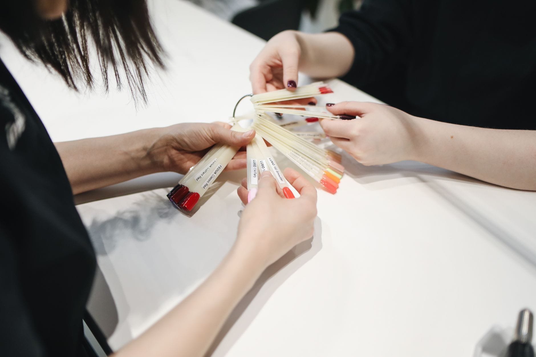 Dłoń klientki wybierająca kolor lakieru z wzornika w salonie manicure