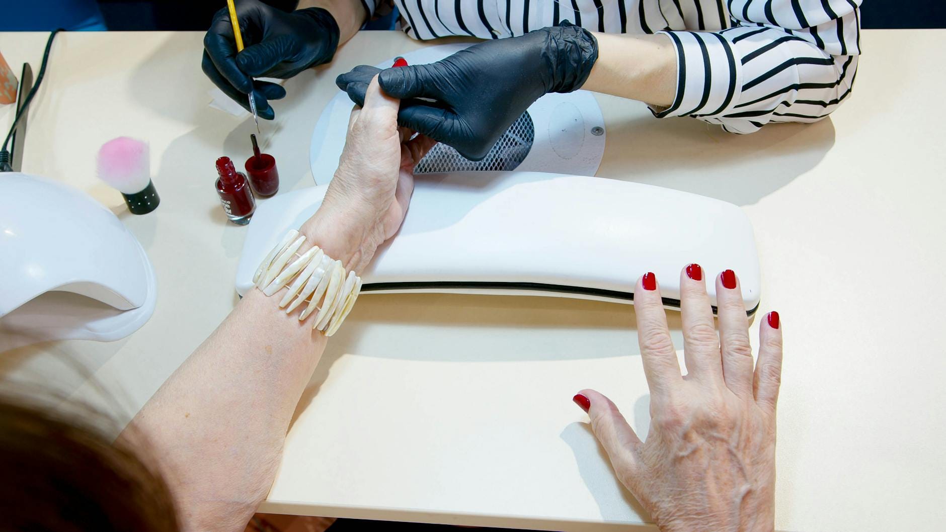 Stylistka nakłada czerwony lakier podczas profesjonalnego manicure