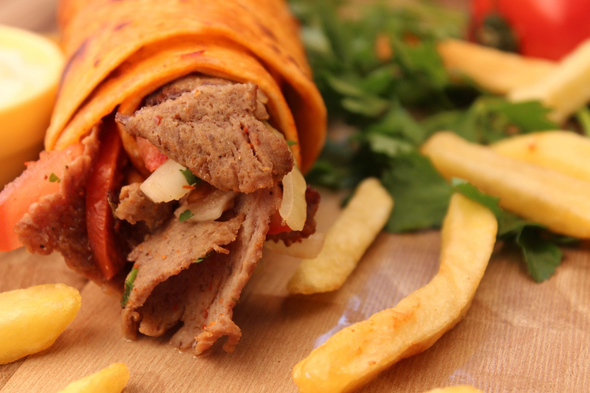 Kebab w bułce z frytkami i ziołami podany na drewnianej desce