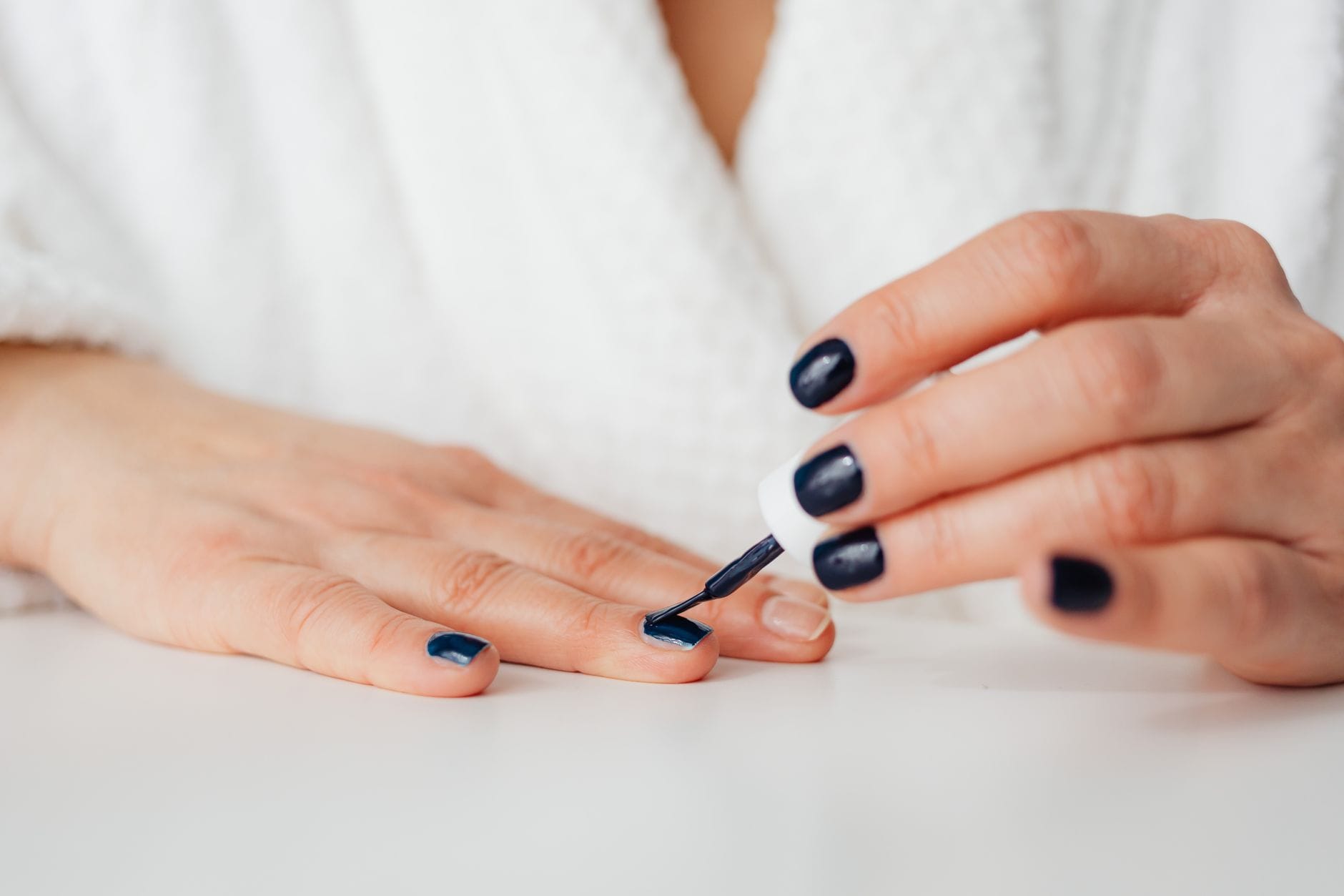 Kobieta maluje w domu paznokcie ciemnym lakierem podczas manicure hybrydowego