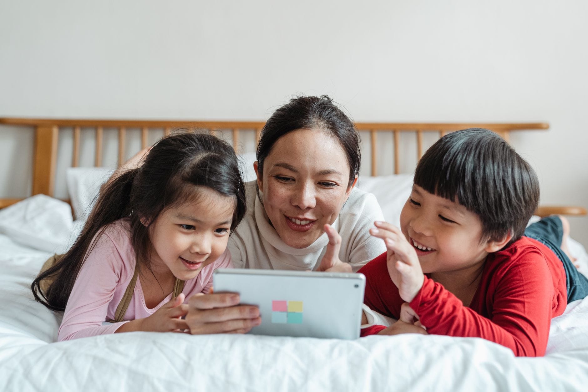 Azjatycka mama z dziećmi na łóżku grająca razem na tablecie