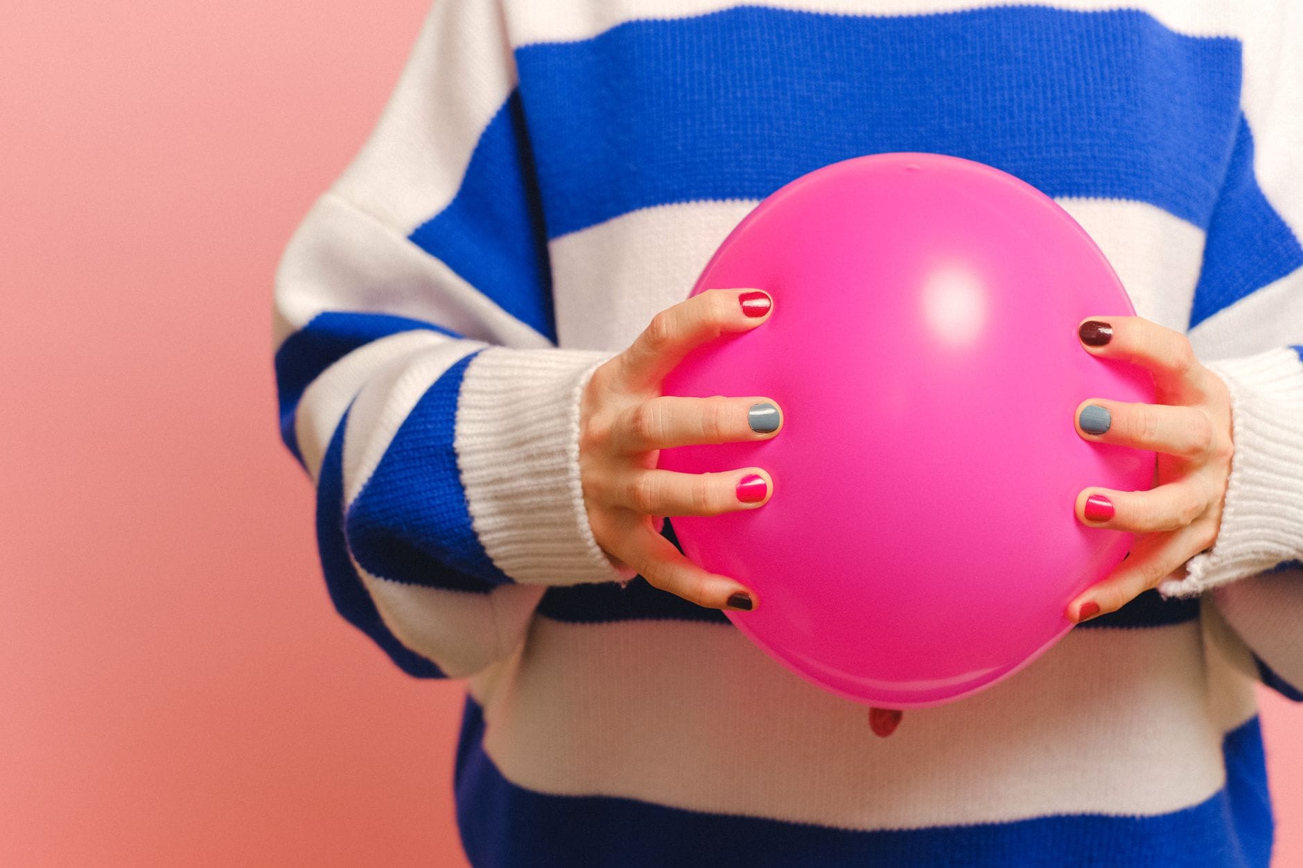 Manicure kombinowany: połączenie frezarki i nożyczek w bezpiecznej kolejności Dłonie z kolorowym manicure trzymające różowy balon na różowym tle
