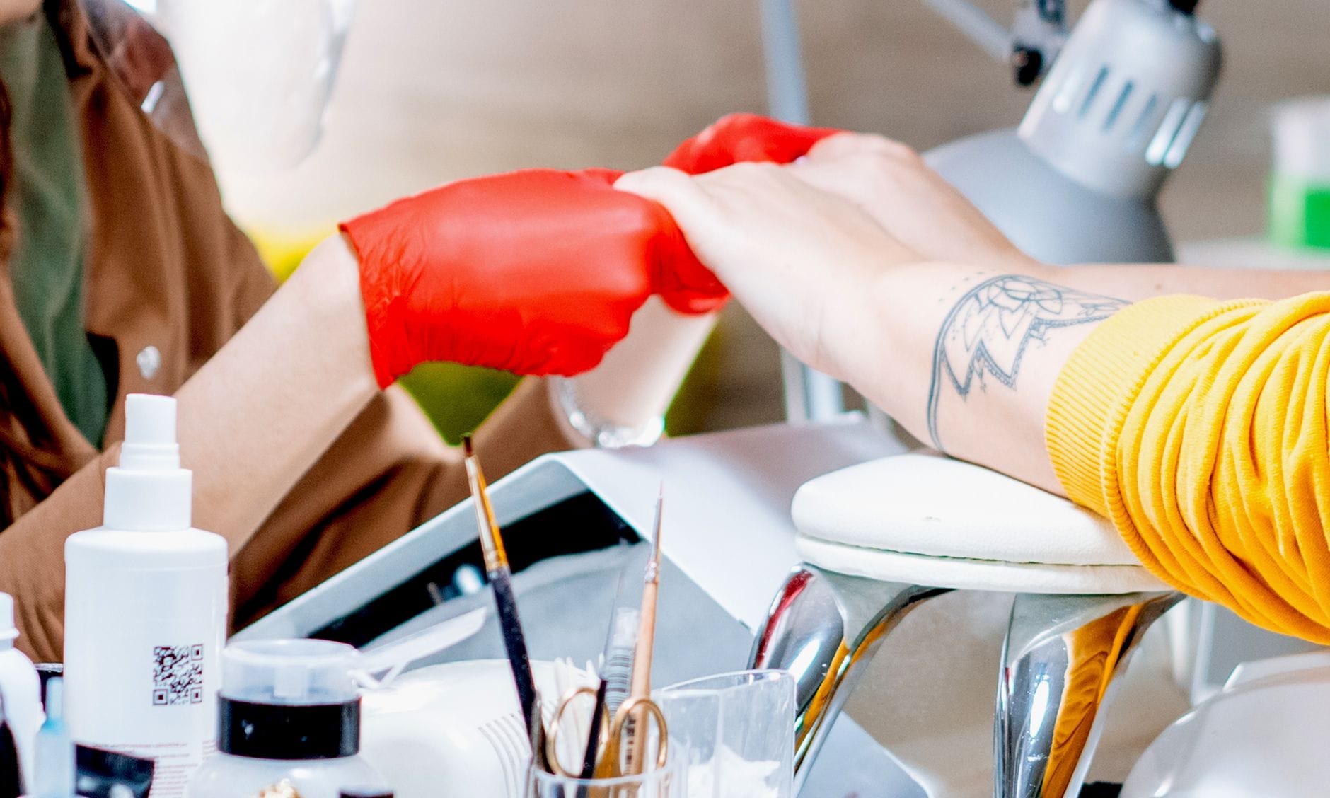 Stylistka w czerwonych rękawiczkach trzyma dłoń klientki podczas manicure
