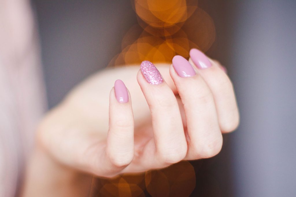 Dłoń kobiety z różowym brokatowym manicure i zdobieniami